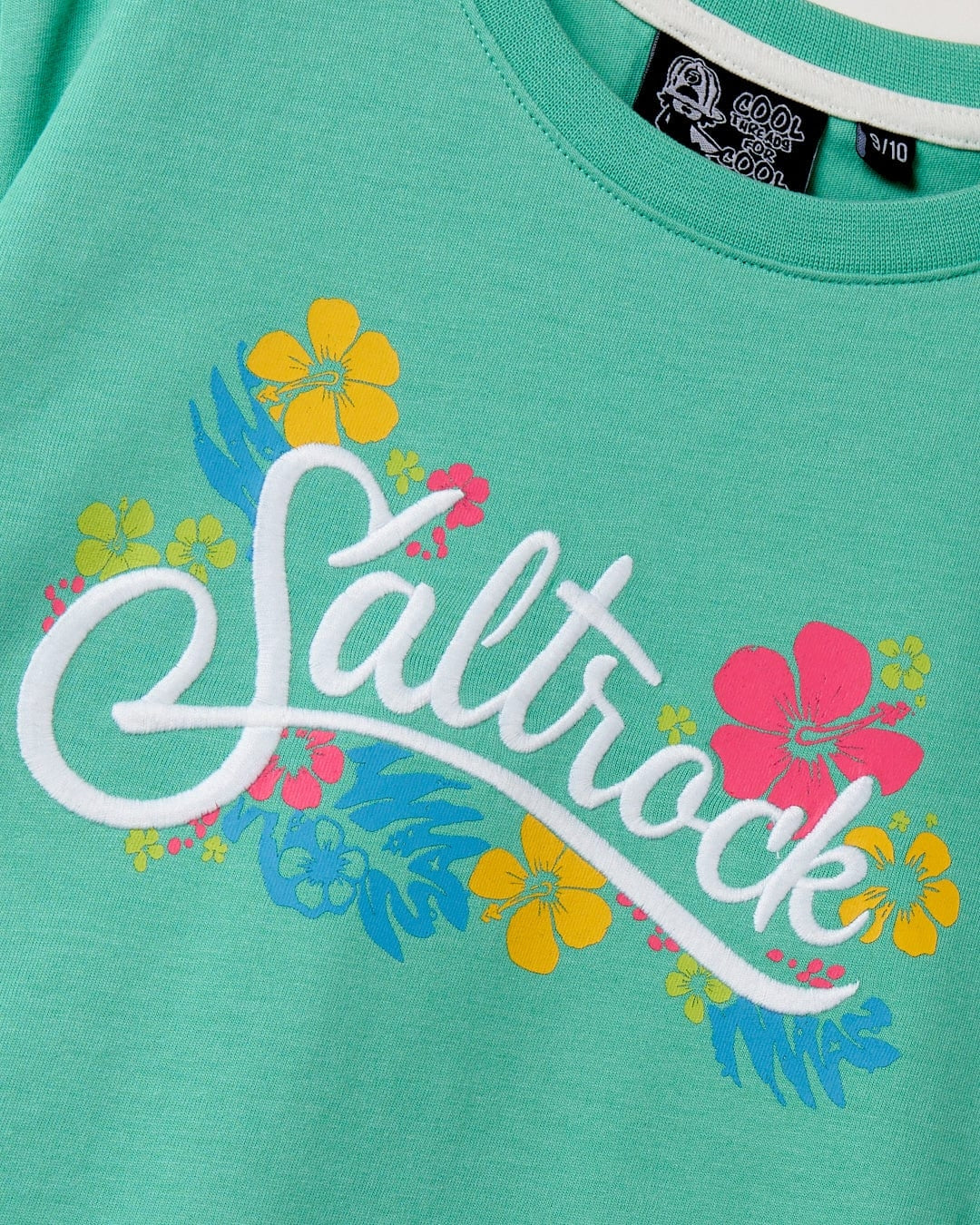 Kids tee from Saltrock in green featuring a multicoloured tropical floral print and embroidered logo on the front.